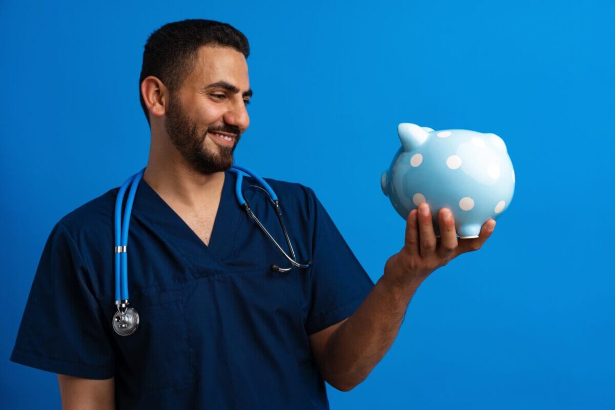 Portrait Of Arab Doctor Holding Piggy Bank On Blue Background