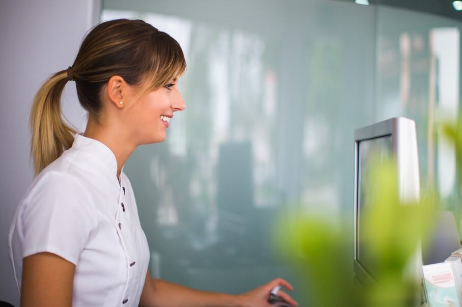 Young Smiling Woman Using Computer At Reception Of Dental Clinic.