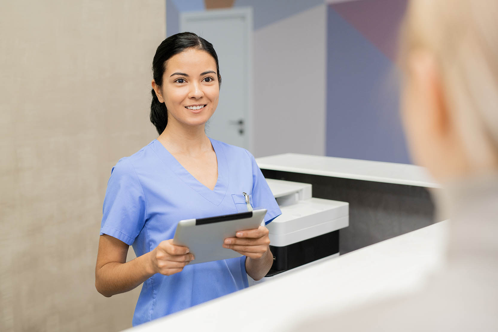 Pretty,Young,Assistant,With,Digital,Tablet,Standing,By,Reception,Counter
