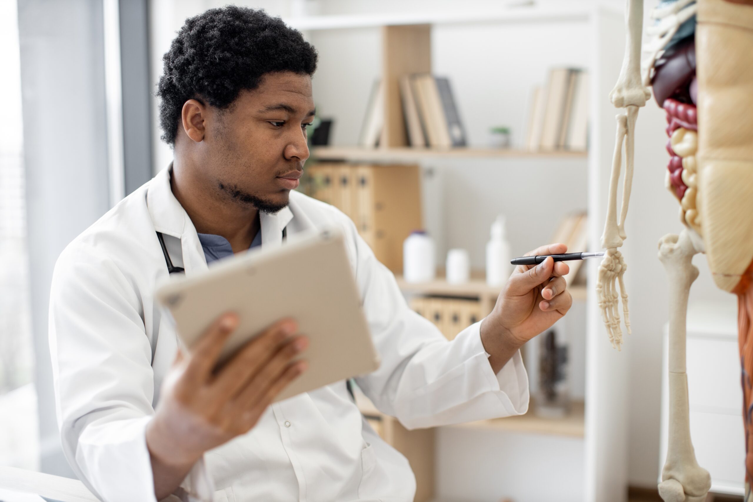 Thoughtful,Multiethnic,Man,In,White,Coat,Indicating,Carpus,Bones,With