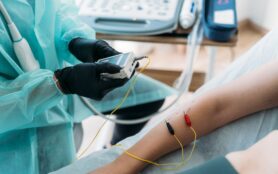 Doctor,Wearing,Protective,Clothes,Examining,Woman's,Arm,With,Electrodes
