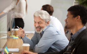 Smiling,Senior,Employee,Discussing,Email,With,African,Colleague,At,Workplace,