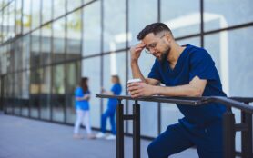 A,Male,Nurse,In,Blue,Scrubs,Appears,Troubled,While,Holding